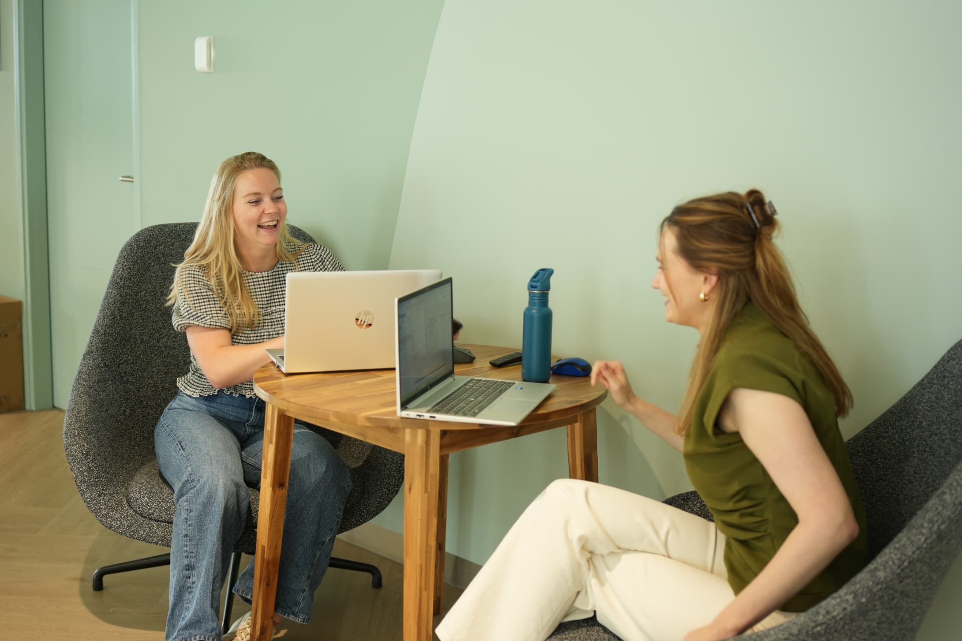 Twee collega's lachen tijdens overleg met laptops